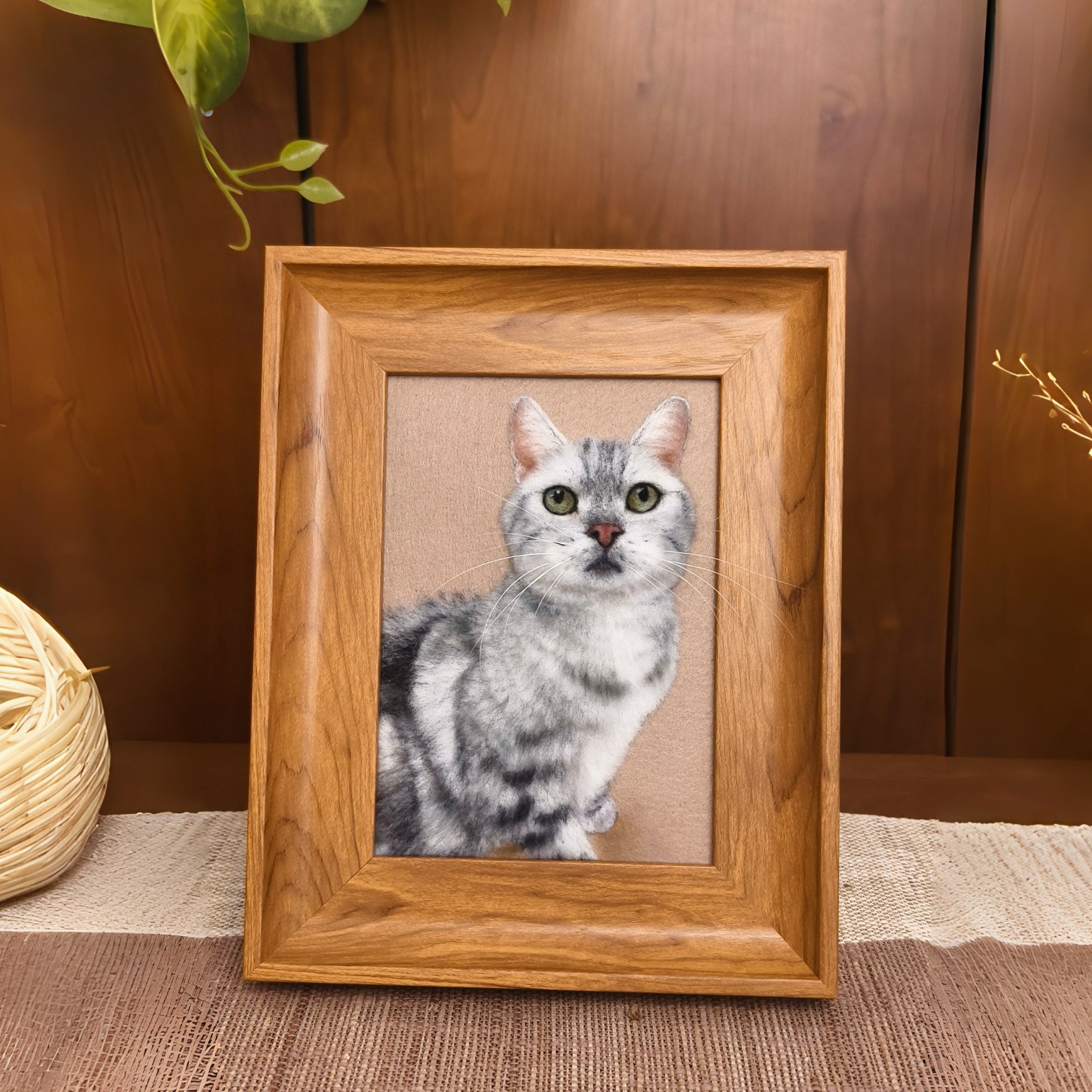 A wooden picture frame, enclosing a portrait of a cat painted on a wool-felt surface